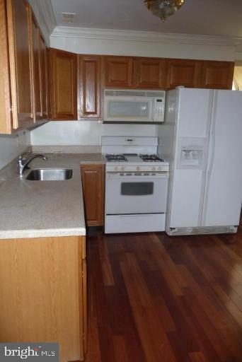 kitchen with dark wood-type flooring, white appliances, sink, and ornamental molding