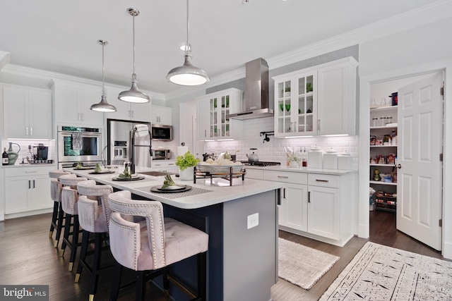 kitchen with appliances with stainless steel finishes, a kitchen island with sink, wall chimney range hood, and white cabinetry