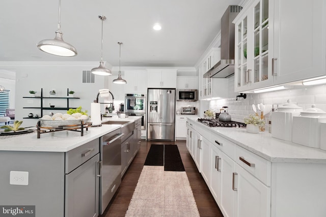 kitchen with pendant lighting, wall chimney range hood, white cabinets, and appliances with stainless steel finishes