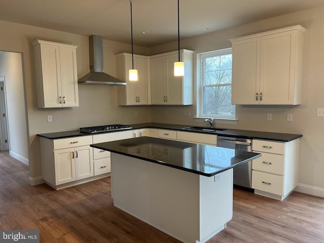 kitchen featuring white cabinetry, stainless steel dishwasher, wall chimney range hood, hanging light fixtures, and light wood-type flooring