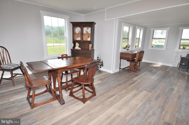 dining room with a wealth of natural light, light hardwood / wood-style flooring, ornamental molding, and a wood stove