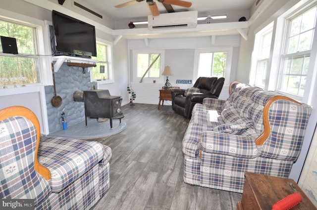 living room with ceiling fan, wood-type flooring, a wall unit AC, and a wood stove