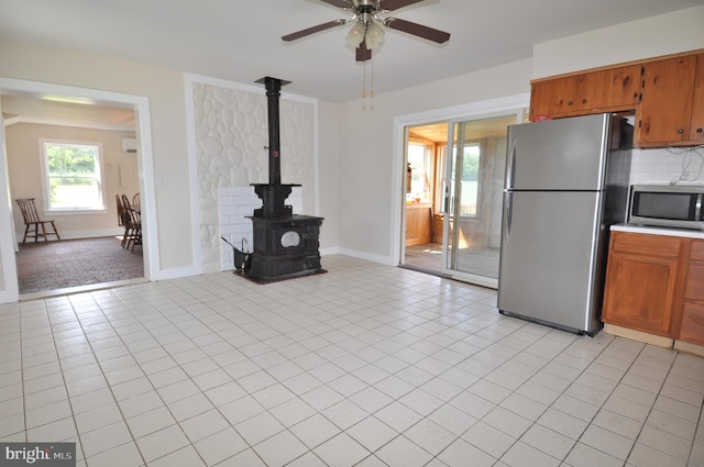 kitchen featuring light tile patterned flooring, a wood stove, ceiling fan, stainless steel appliances, and decorative backsplash