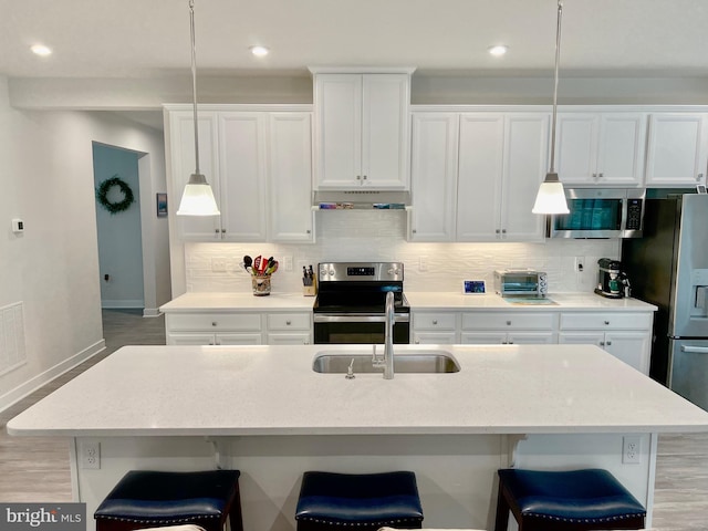 kitchen featuring pendant lighting, stainless steel appliances, an island with sink, and white cabinets