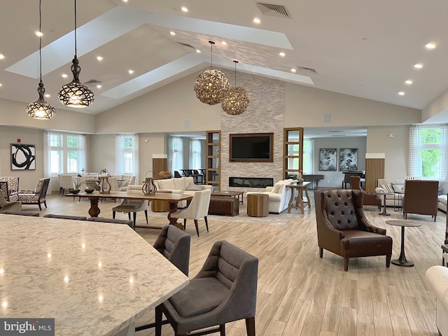 dining room featuring high vaulted ceiling, a stone fireplace, and light hardwood / wood-style floors