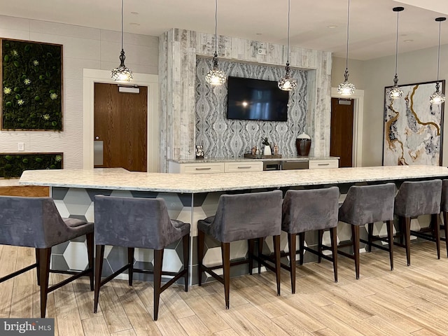 bar with white cabinetry, hanging light fixtures, light stone countertops, and light wood-type flooring