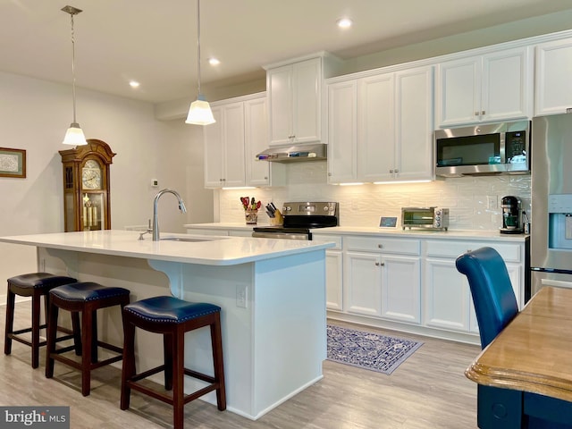 kitchen with appliances with stainless steel finishes, decorative light fixtures, white cabinets, backsplash, and a center island with sink