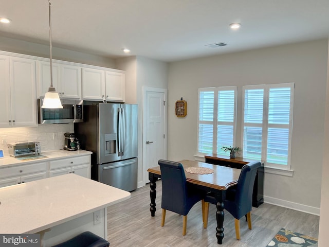 kitchen featuring hanging light fixtures, light hardwood / wood-style flooring, white cabinets, stainless steel appliances, and backsplash