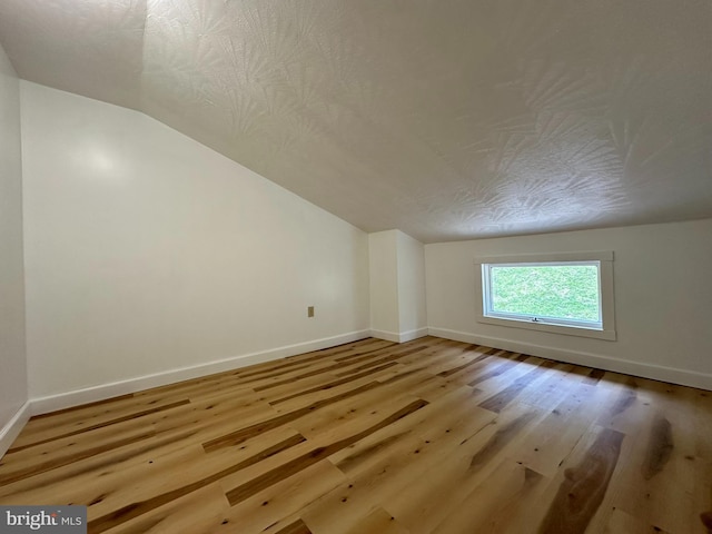 additional living space featuring a textured ceiling, lofted ceiling, and light wood-type flooring