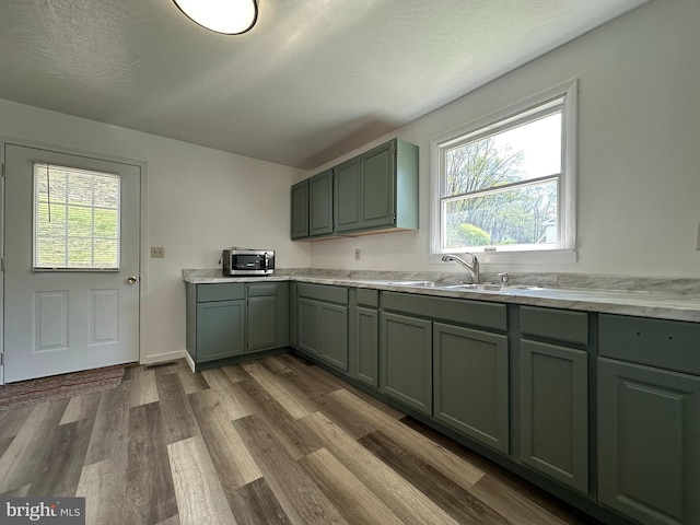 kitchen featuring a textured ceiling, green cabinets, wood-type flooring, and sink