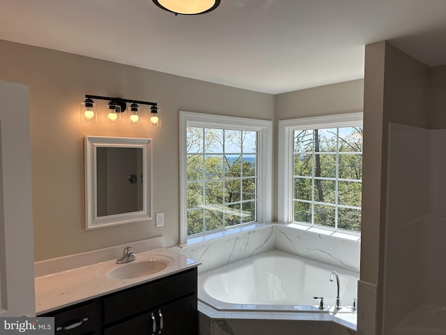 bathroom with tiled tub, vanity, and a healthy amount of sunlight