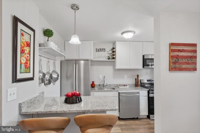 kitchen with appliances with stainless steel finishes, white cabinetry, a breakfast bar, kitchen peninsula, and light wood-type flooring