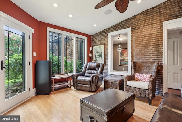 sitting room with ceiling fan, brick wall, lofted ceiling, and light wood-type flooring