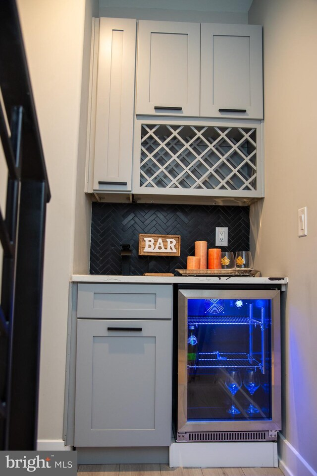 bar featuring gray cabinets, backsplash, and beverage cooler