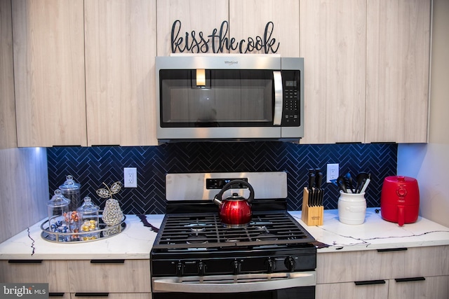 kitchen with light brown cabinets, light stone counters, stainless steel appliances, and backsplash