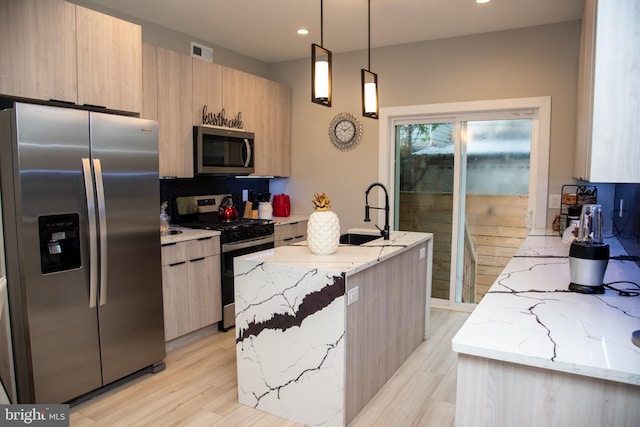 kitchen with stainless steel appliances, hanging light fixtures, light hardwood / wood-style floors, light stone countertops, and an island with sink