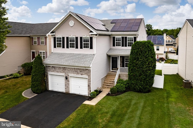 view of front of home featuring a garage, a front lawn, solar panels, and central AC unit