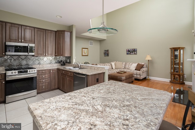 kitchen with dark brown cabinetry, sink, appliances with stainless steel finishes, kitchen peninsula, and backsplash