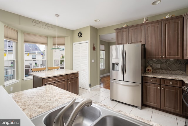 kitchen with dark brown cabinetry, stainless steel fridge with ice dispenser, hanging light fixtures, light tile patterned floors, and backsplash