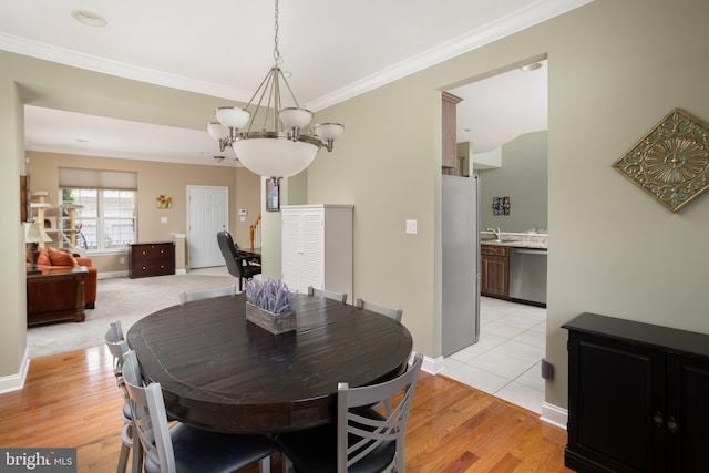 dining area with an inviting chandelier, sink, crown molding, and light hardwood / wood-style floors