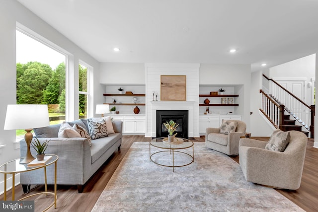 living room with built in shelves, a fireplace, and wood-type flooring