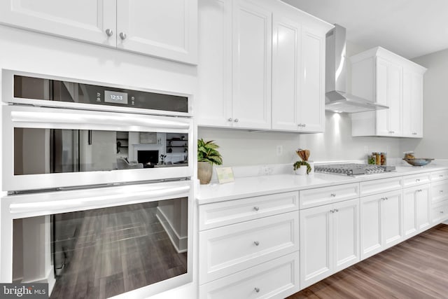 kitchen featuring wall chimney range hood, white cabinets, dark hardwood / wood-style floors, and stainless steel appliances