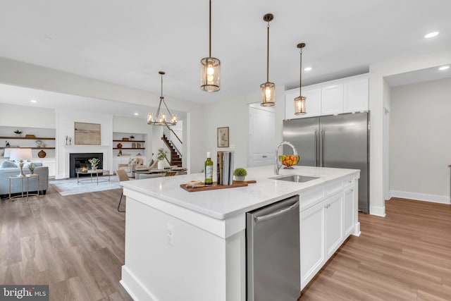 kitchen with built in shelves, white cabinets, a kitchen island with sink, and stainless steel appliances