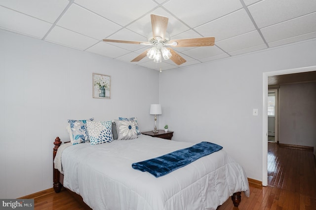 bedroom with ceiling fan, baseboard heating, wood-type flooring, and a paneled ceiling