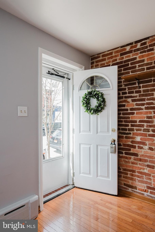 foyer entrance with light wood-type flooring, a baseboard heating unit, and brick wall