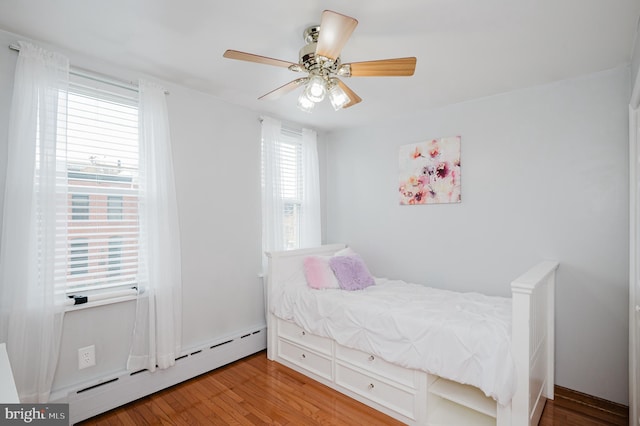 bedroom with ceiling fan, a baseboard heating unit, and wood-type flooring