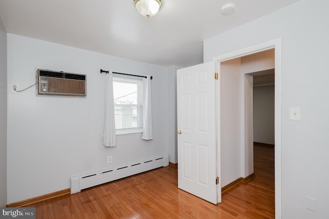 unfurnished bedroom featuring baseboard heating, wood-type flooring, and a wall mounted AC