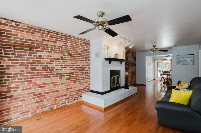 unfurnished living room with rail lighting, hardwood / wood-style flooring, ceiling fan, brick wall, and a fireplace