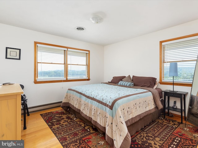 bedroom with a baseboard heating unit, light hardwood / wood-style floors, and multiple windows