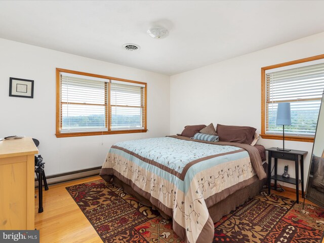 bedroom with multiple windows, baseboard heating, and light wood-type flooring