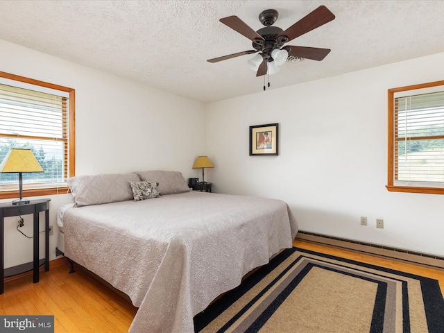 bedroom featuring light hardwood / wood-style floors, multiple windows, baseboard heating, and ceiling fan