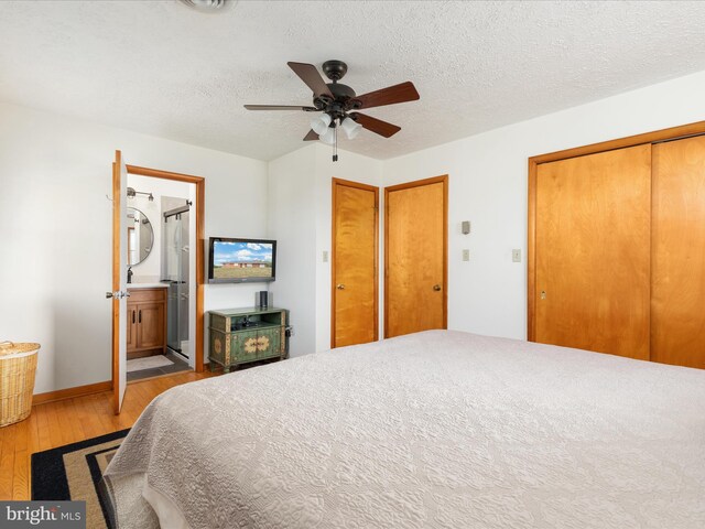 bedroom with ensuite bathroom, light wood-type flooring, ceiling fan, and a textured ceiling