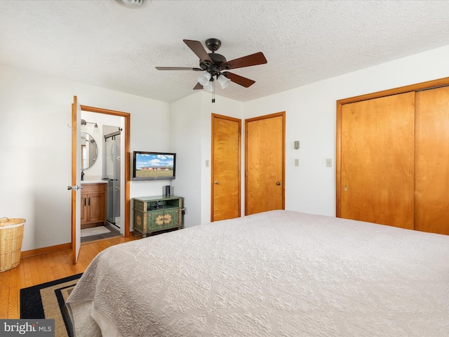 bedroom featuring ensuite bath, ceiling fan, a textured ceiling, multiple closets, and light wood-type flooring