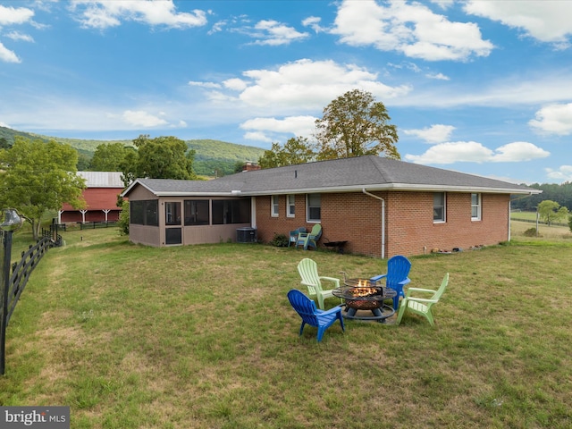 rear view of house with central AC, a yard, a mountain view, a fire pit, and a sunroom