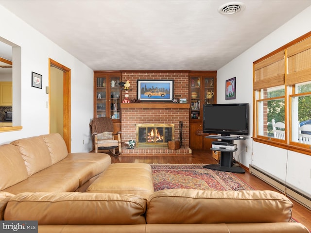 living room with brick wall, a fireplace, baseboard heating, and hardwood / wood-style floors