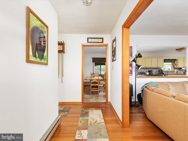 hall featuring a baseboard radiator, a healthy amount of sunlight, and light hardwood / wood-style flooring