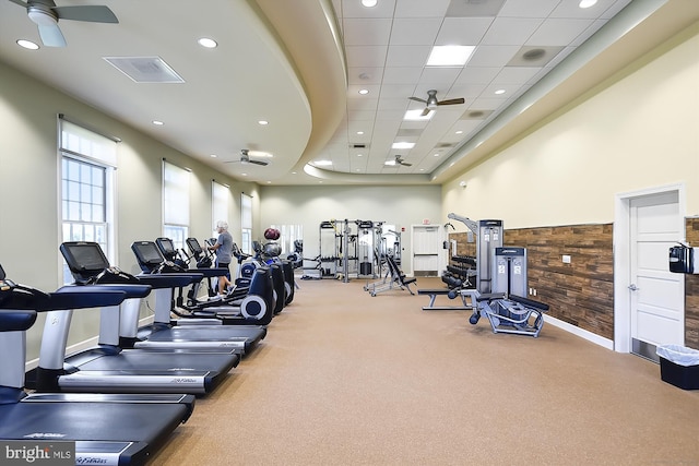 exercise room with a drop ceiling, wooden walls, ceiling fan, and a high ceiling