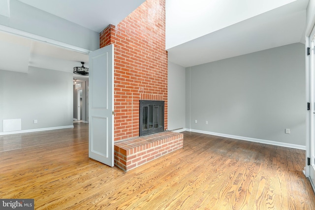 unfurnished living room with lofted ceiling, a fireplace, and light hardwood / wood-style floors