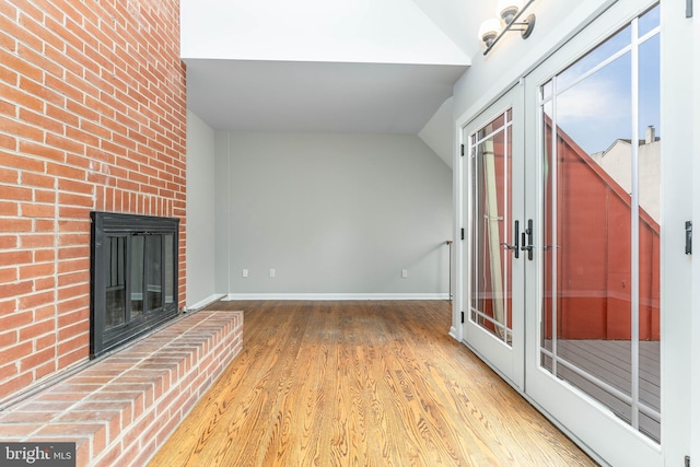 unfurnished living room featuring hardwood / wood-style floors, french doors, a fireplace, and vaulted ceiling