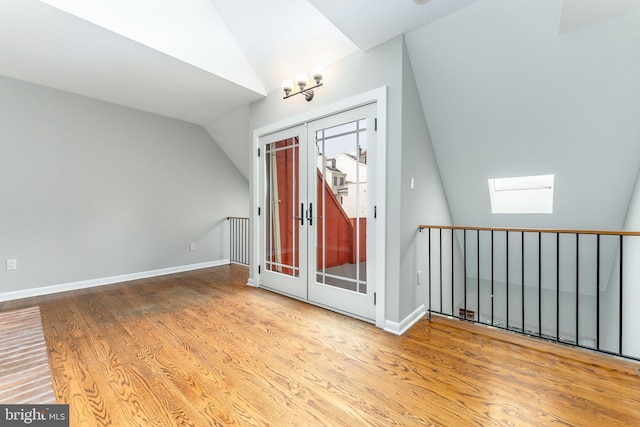 foyer with wood-type flooring, french doors, and vaulted ceiling with skylight