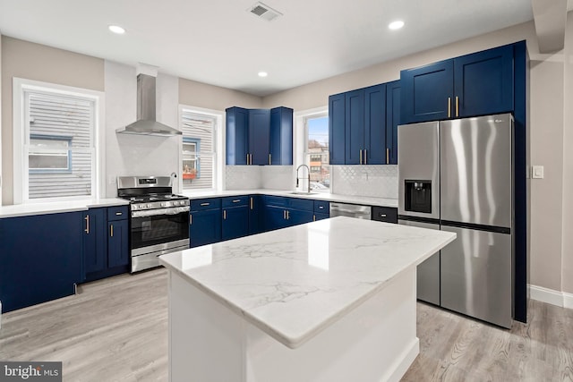 kitchen with wall chimney range hood, visible vents, blue cabinetry, and stainless steel appliances