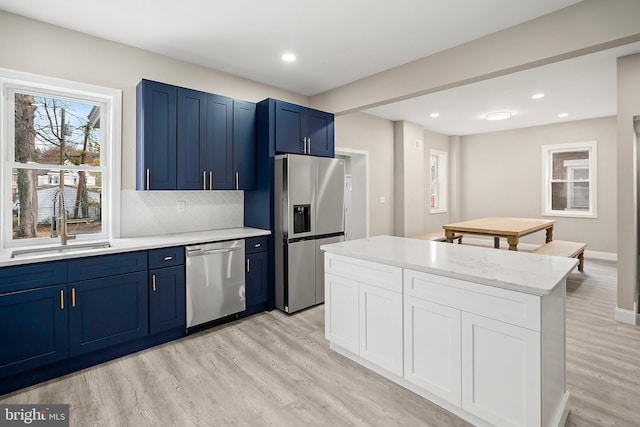 kitchen with blue cabinetry, light wood-type flooring, appliances with stainless steel finishes, and a sink