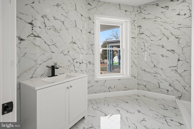 bathroom featuring marble finish floor, stone wall, and vanity