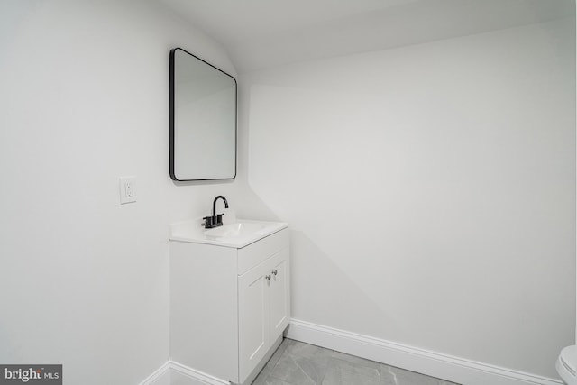 bathroom featuring baseboards, toilet, lofted ceiling, marble finish floor, and vanity