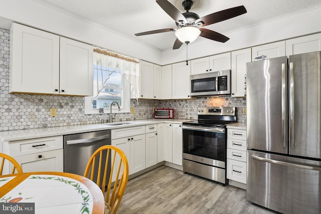 kitchen featuring appliances with stainless steel finishes, light hardwood / wood-style flooring, tasteful backsplash, white cabinetry, and ceiling fan