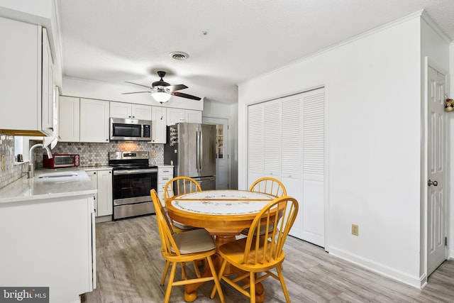 dining area with light wood-type flooring, a textured ceiling, ceiling fan, sink, and ornamental molding